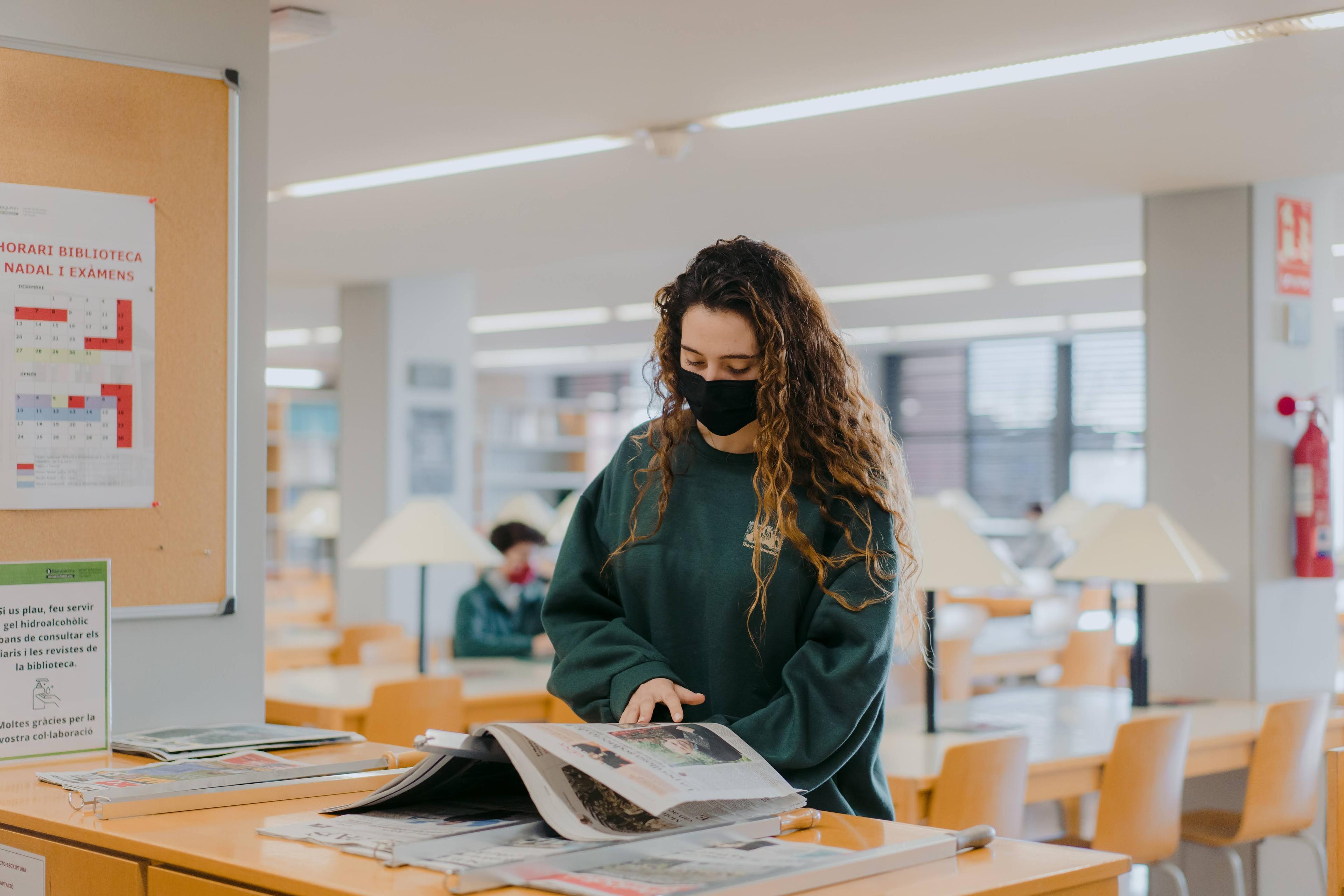 Alumna llegint un diari a la biblioteca